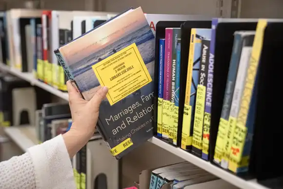 A close-up of a hand pulling a textbook off of a library shelf