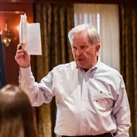 Tom Heuer holds up a book as he speaks to students seated at tables in the Shriver Center at Miami University. A projector screen behind him displays a slide with the words: Your Values and Your Vision.