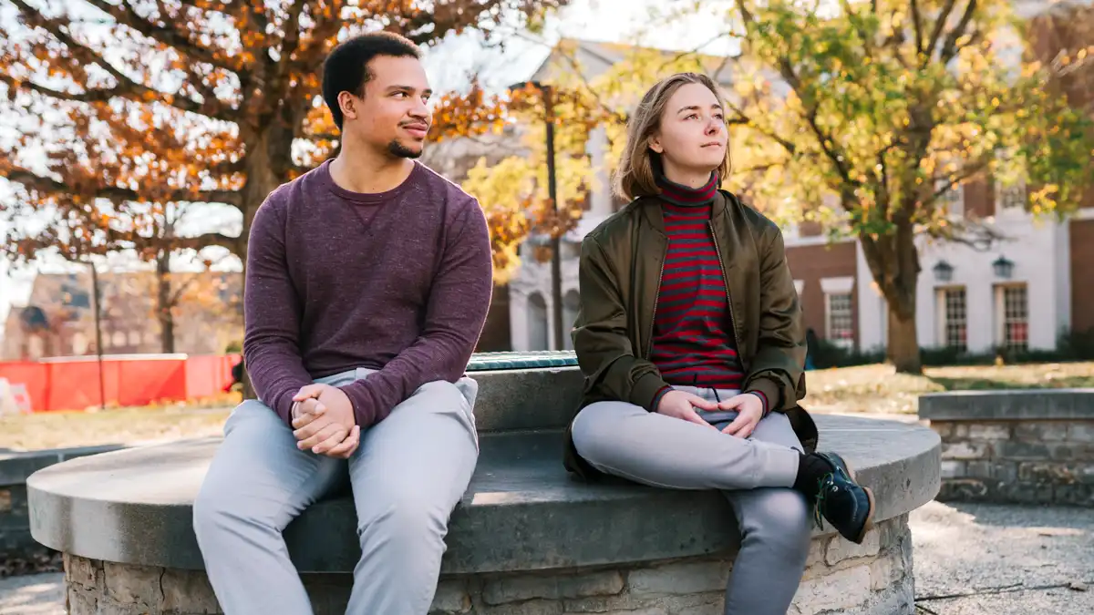 Romero Pearson and Hal Howard sit on a stone bench outside King LIbrary in the fall.